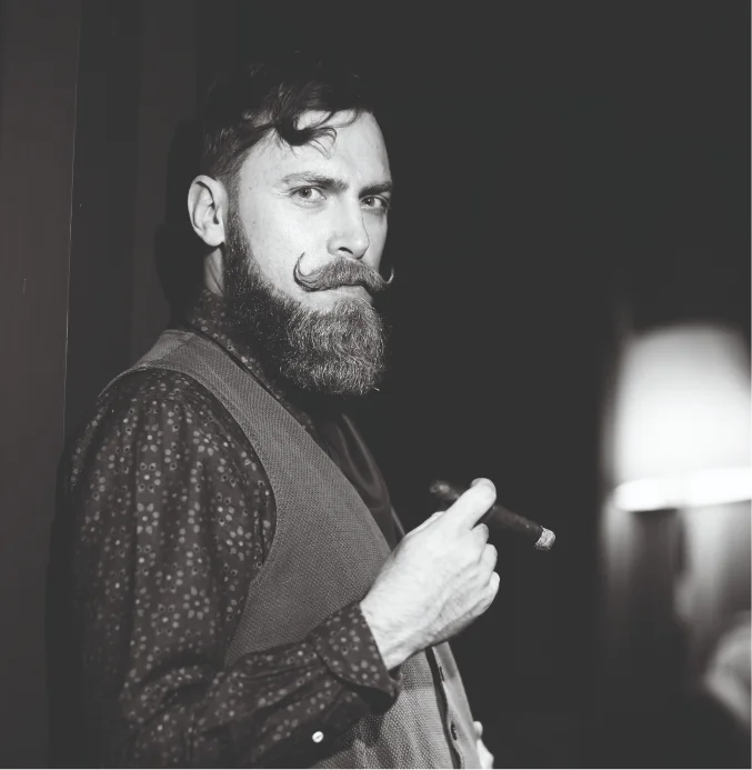 Bearded man with styled moustache holding cigar – TheBarber.ch quick cosmetics men's facial skin care service Zurich
