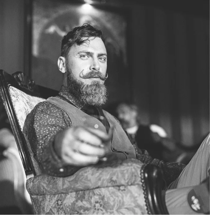 Relaxed bearded man with styled moustache sitting in armchair – TheBarber.ch Relax hand bath cuticle care and exfoliation Zurich